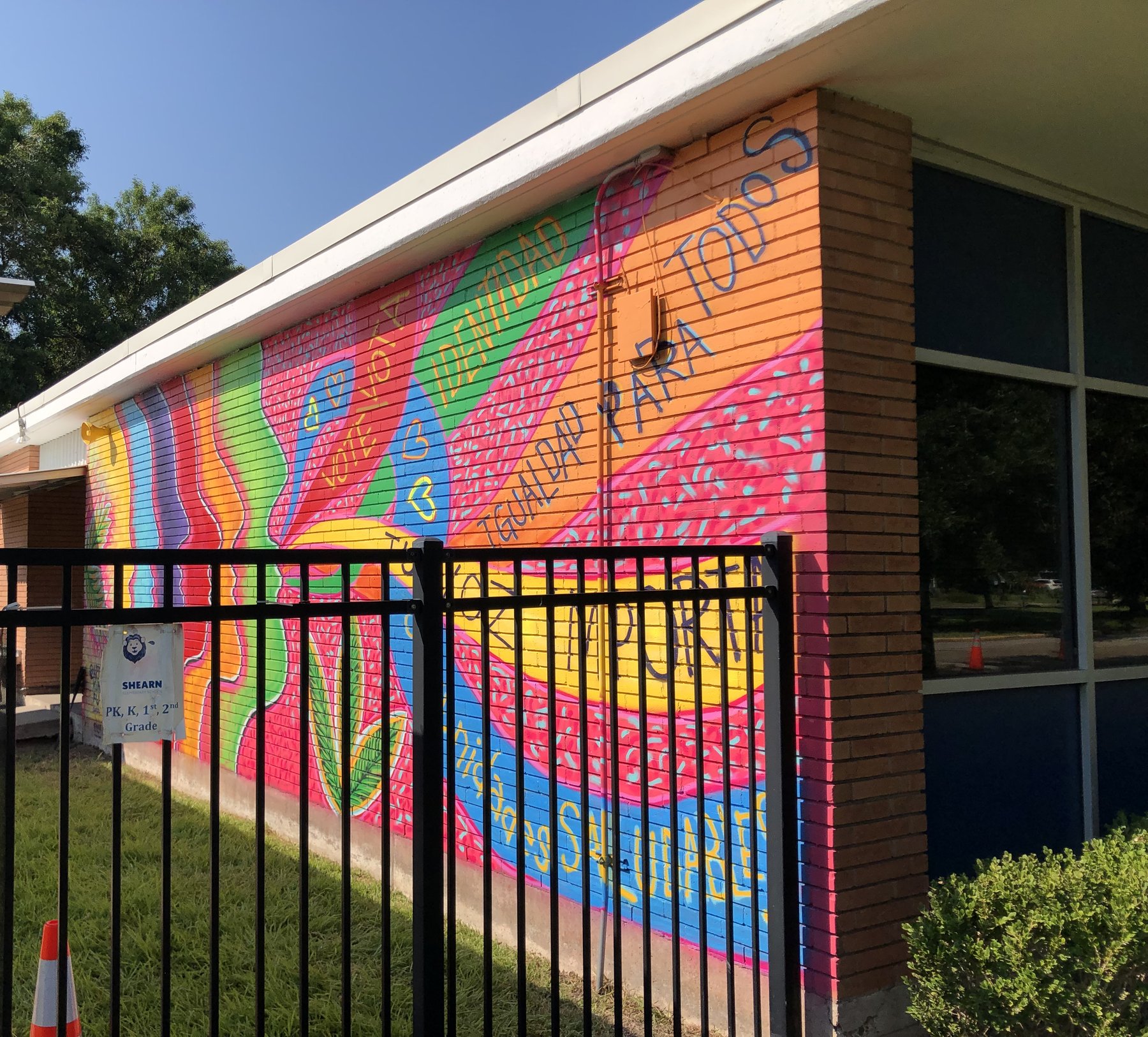 A long school wall painted with rainbow bands, faces in profile and the words Tu voz importa