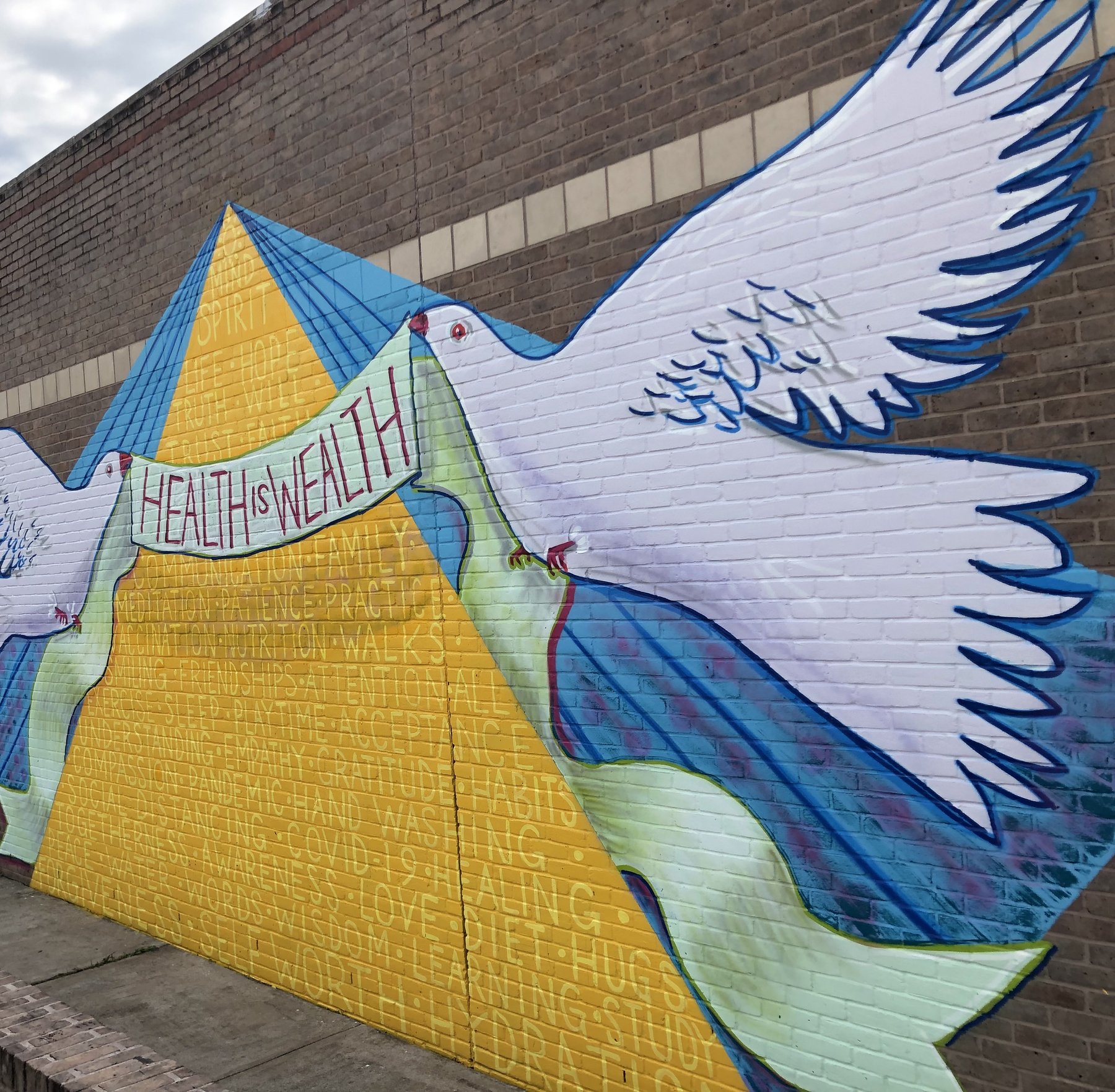 A mural of two doves carrying a banner reading Health is Wealth, painted on a school wall