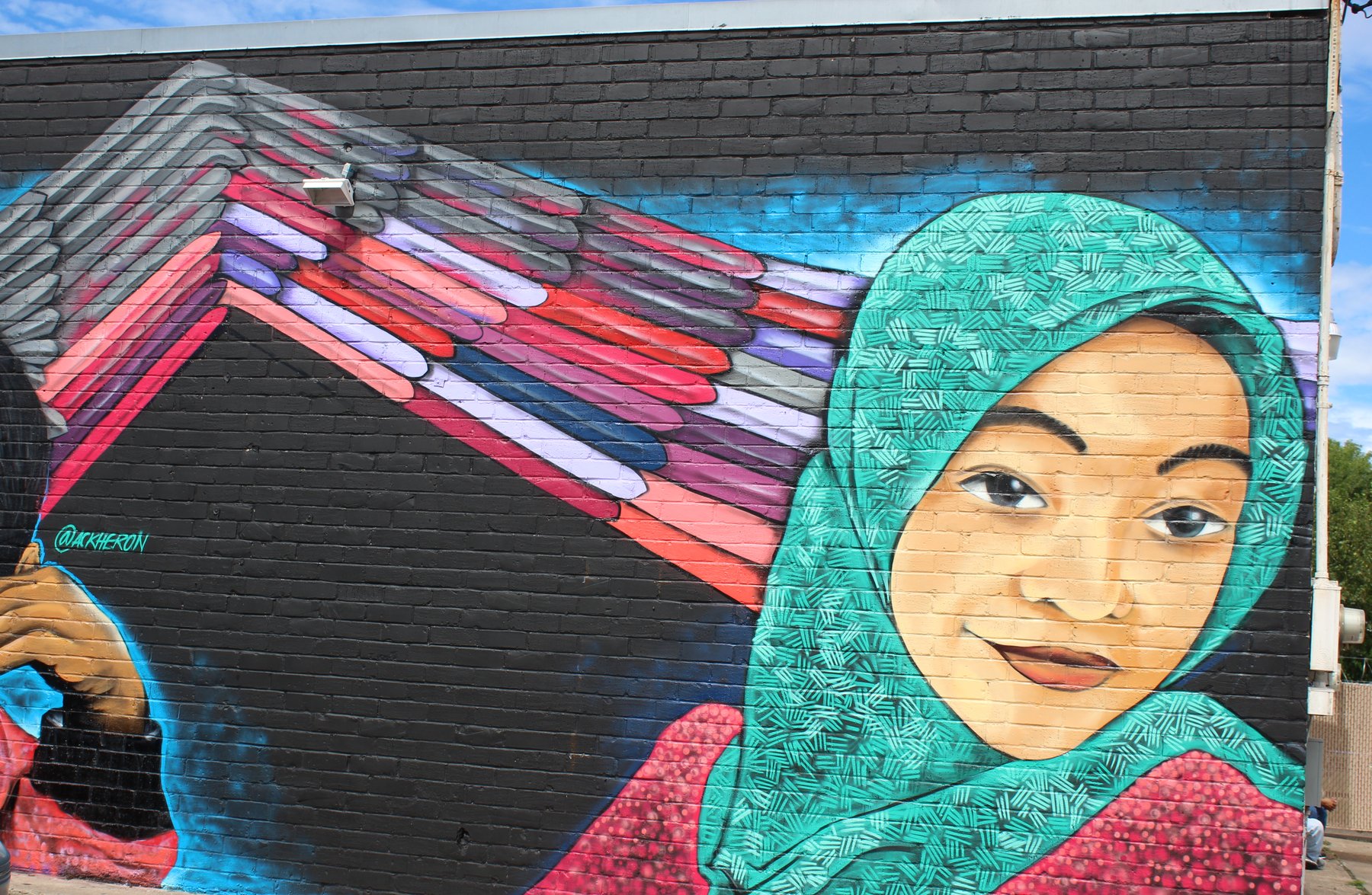 A mural of two young women with painted wings spread behind them, on a black brick wall