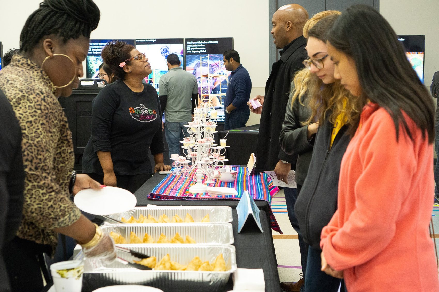 People gathered around a table of food with mural displays behind them